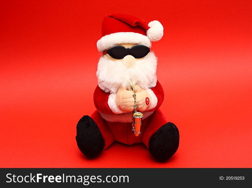 Soft toy Santa Claus wearing shades and playing saxophone on red background. Soft toy Santa Claus wearing shades and playing saxophone on red background
