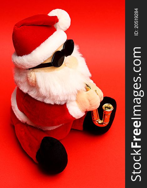 Soft toy Santa Claus wearing shades and playing saxophone on red background