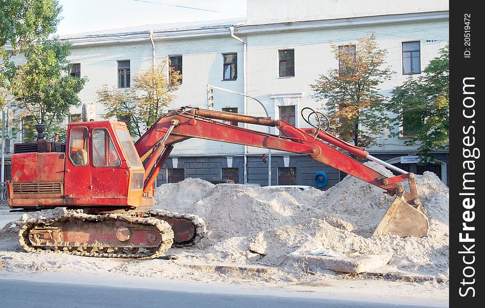 Red excavator with tracks at road repairing works