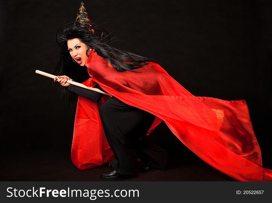 Female in witch costume with red cloak and broom between her legs screaming. Female in witch costume with red cloak and broom between her legs screaming