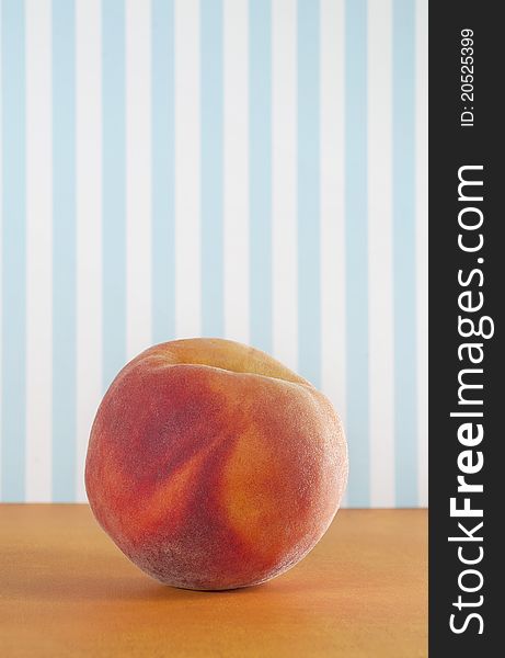 One peach on an orange table against an old-fashioned blue-white striped wallpaper. One peach on an orange table against an old-fashioned blue-white striped wallpaper.