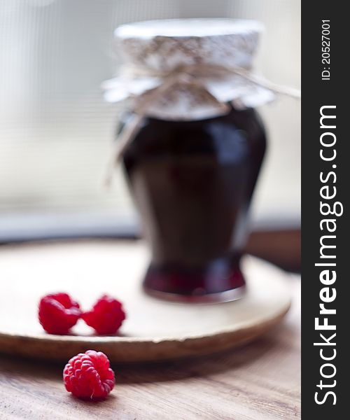 Jar of raspberry jam, three fruit in front,