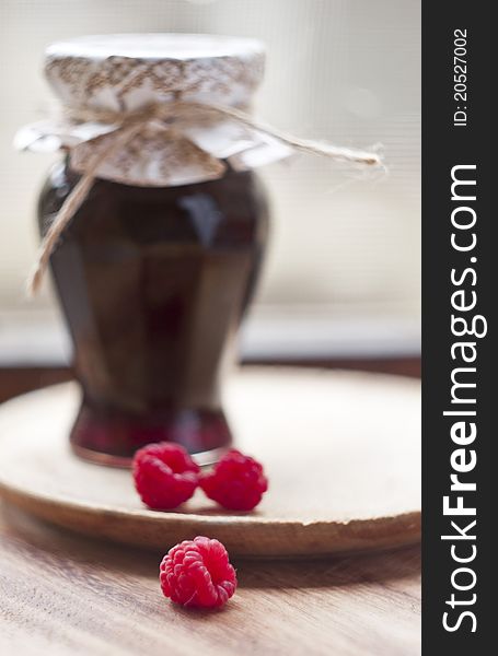 Jar of raspberry jam, three fruit in front,