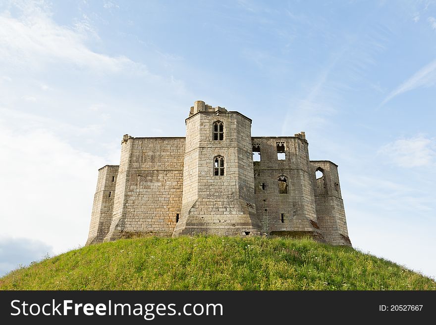 The ruins of an English castle sit on the top of a mound of grass. The ruins of an English castle sit on the top of a mound of grass.