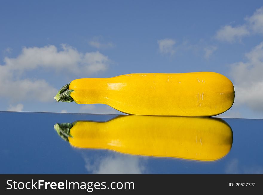 Yellow courgette on mirror and blue sky