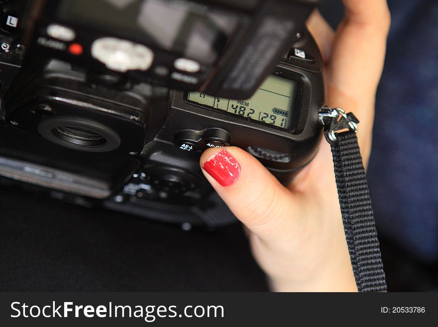 A woman's hand with red painted nails is holding a professional photographic camera. A woman's hand with red painted nails is holding a professional photographic camera