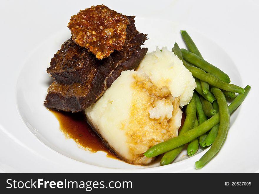 Braised pork belly garnished with pork crackling served with a rich jus, mashed potatoes and green beans