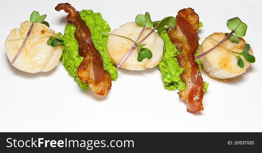 Pan-fried scallops with pea puree and bacon slices garnished with micro herbs. Pan-fried scallops with pea puree and bacon slices garnished with micro herbs