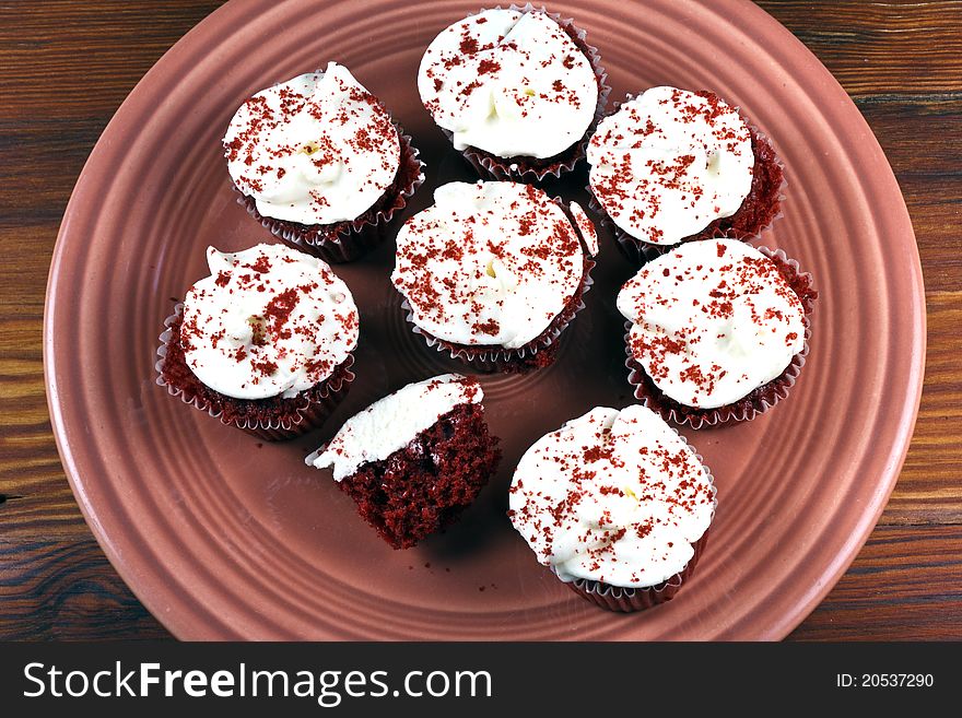 Red Velvet Cupcakes with frosting on a mauve plate and on a wooden table.