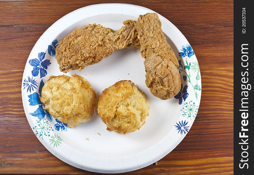 Fried chicken and biscuits on a paper plate and wood table.