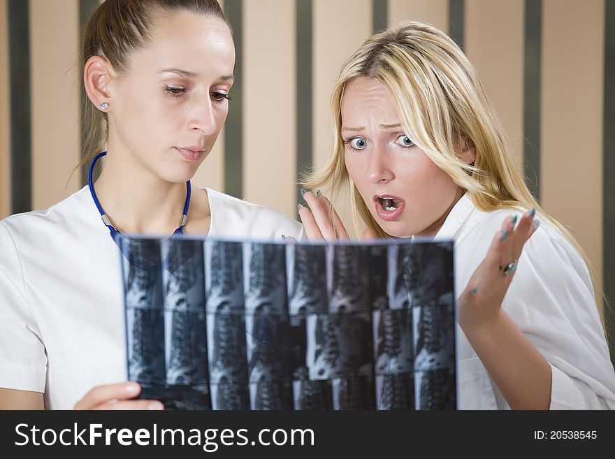 Two women doctors reading radiology scans of patient spine - shocked diagnosis scene. Two women doctors reading radiology scans of patient spine - shocked diagnosis scene.