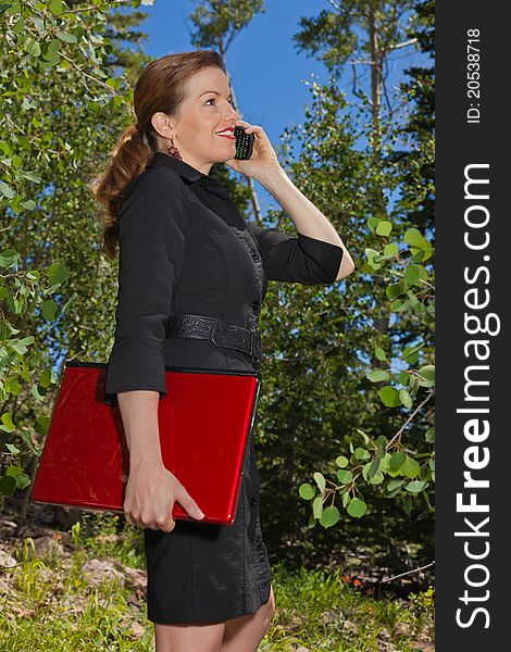 Business woman in the forest talking on her cell phone holding a laptop. Business woman in the forest talking on her cell phone holding a laptop.