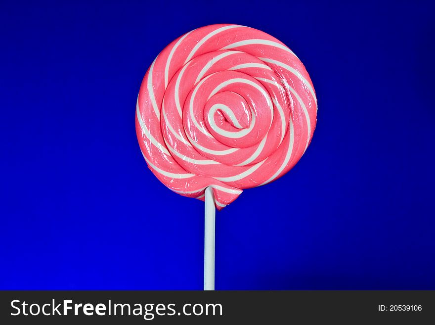 Lovely lollipop with pink and white stripes on blue background.