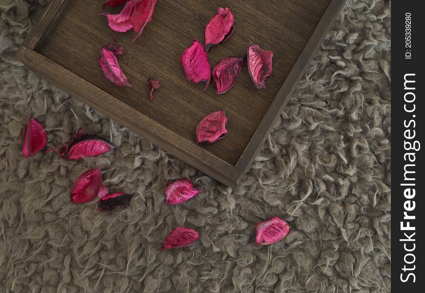 Dry petals of red roses are on a wooden box and soft brown carpet