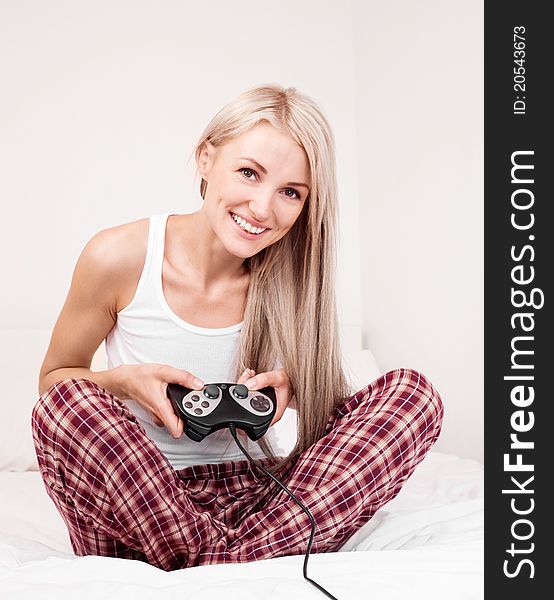 Beautiful young blond woman playing computer games on the bed at home