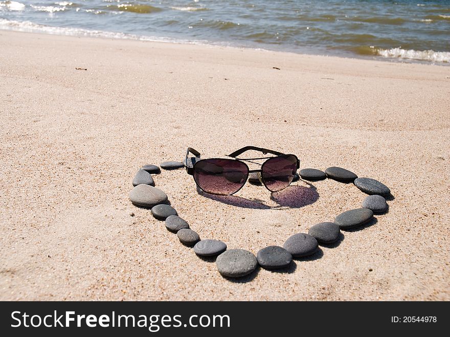 Heart made from stones and sunglasses on the beach