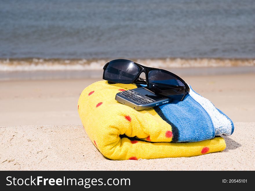 Towel, mobile phone and sunglasse on the seashore