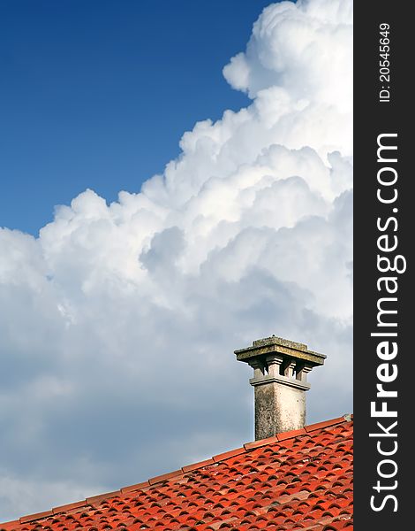 A chimney on a roof of a house with blue sky covered with clouds. A chimney on a roof of a house with blue sky covered with clouds