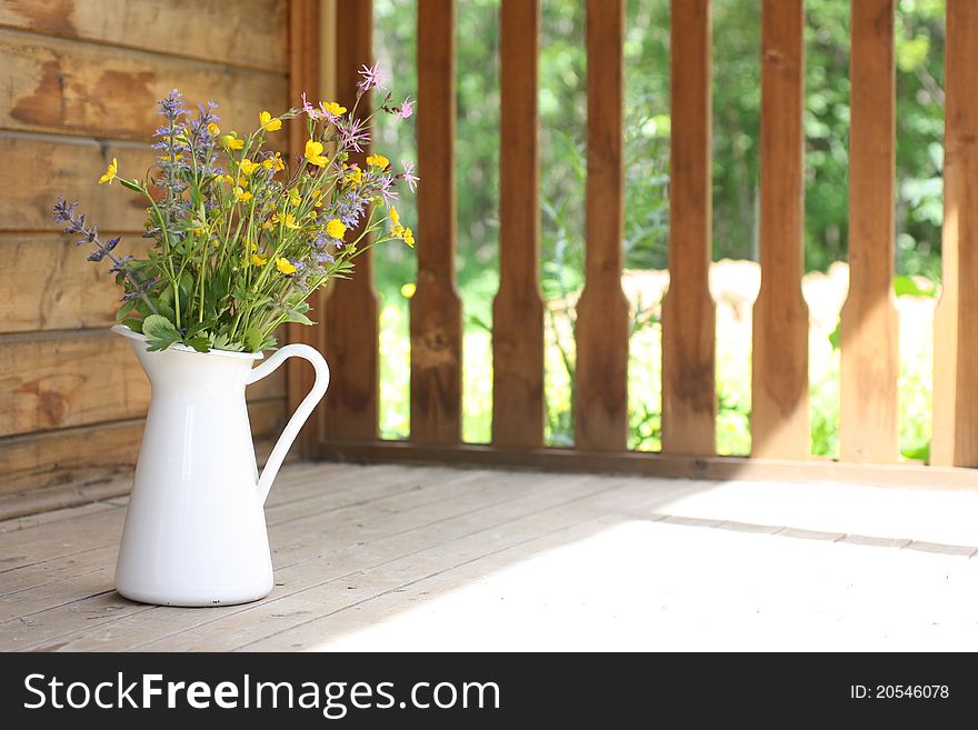 Summer bouquet in a white pitcher on wooden terrace