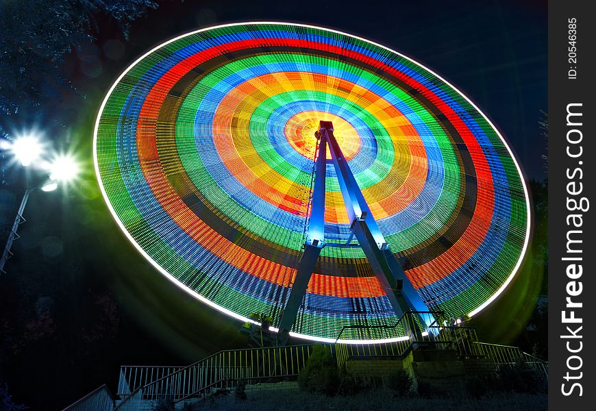 Ferris wheel rotates at night and the lights are merged into multi-colored circles.