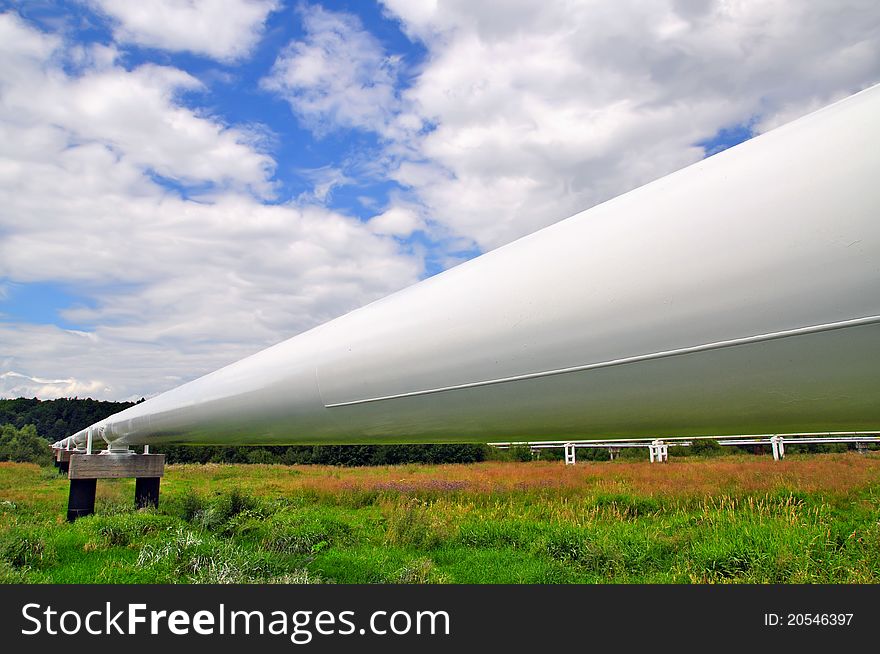 The high pressure pipeline in a summer landscape with the dark blue sky and clouds.