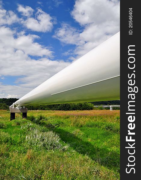 The high pressure pipeline in a summer landscape with the dark blue sky and clouds.