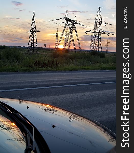 High voltage electricity pylon over sunset and reflection in car