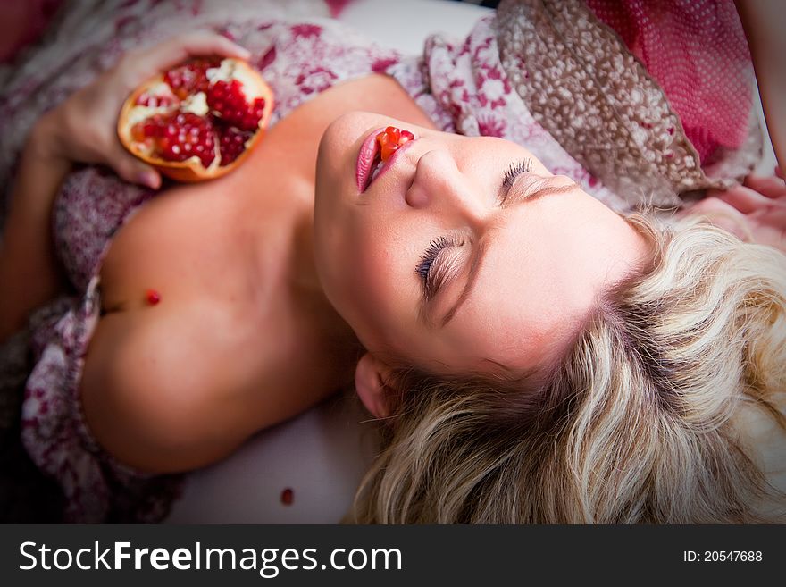 Portrait of beautiful lying blonde woman with closed eyes holding half of pomegranate. Portrait of beautiful lying blonde woman with closed eyes holding half of pomegranate