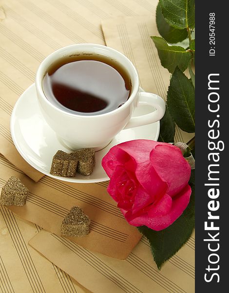 White cup of tea next to sugar and is a beautiful red rose lying on sheets of old paper sheet music. White cup of tea next to sugar and is a beautiful red rose lying on sheets of old paper sheet music