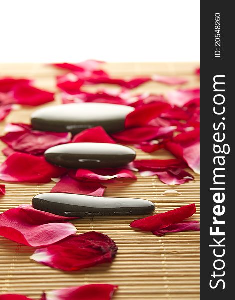 Close-up of three polished stones lie strewn on a wooden surface with rose petals. Close-up of three polished stones lie strewn on a wooden surface with rose petals