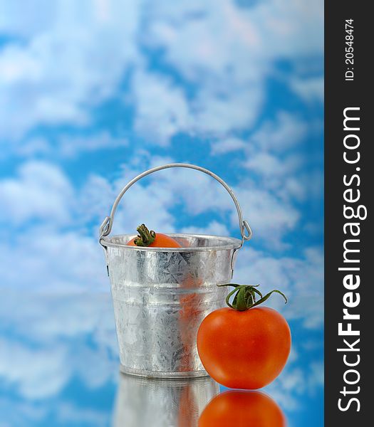 Tomato in silver bucket with reflection clouds and glass