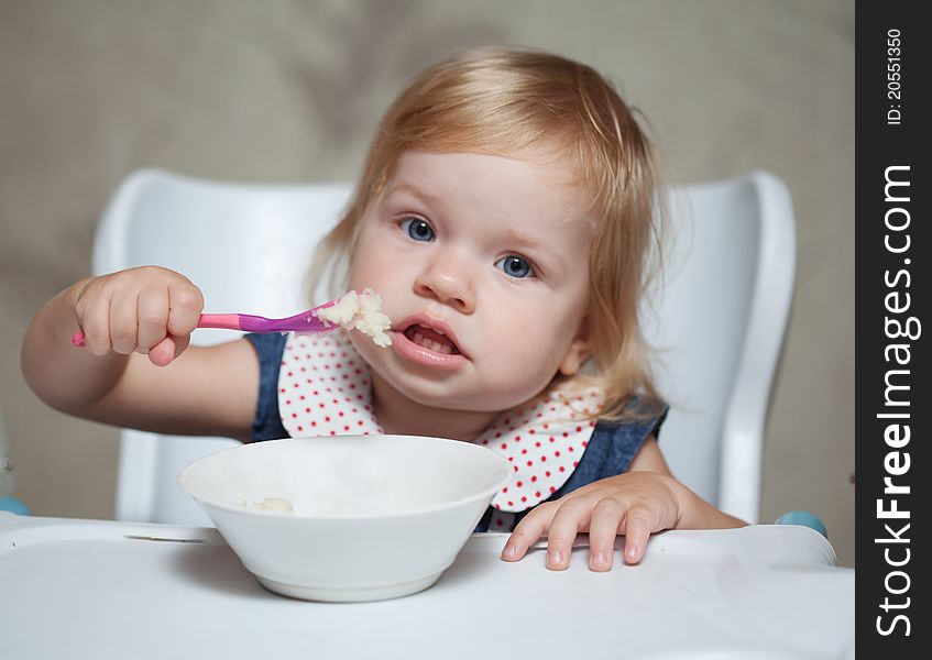 Baby sitting in the baby seat and eating porridge. focus on hand with spoon. Baby sitting in the baby seat and eating porridge. focus on hand with spoon
