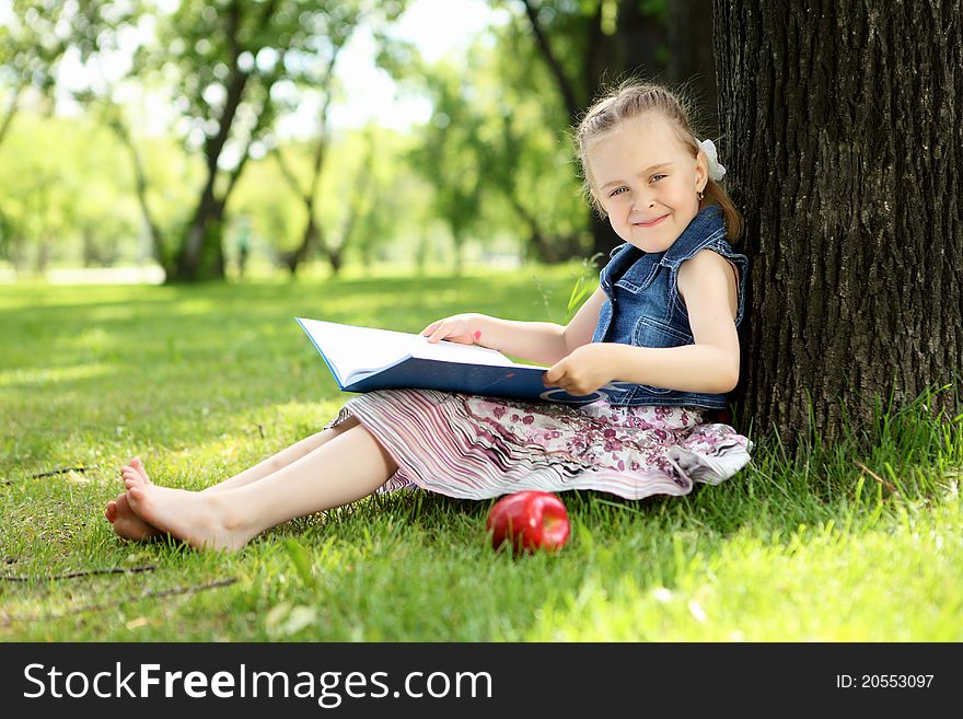 Portrait of a little girl sitting and reading on the grass in the park. Portrait of a little girl sitting and reading on the grass in the park