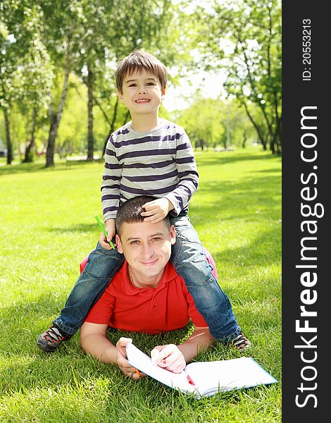 Father with his son reading together in the summer park. Father with his son reading together in the summer park