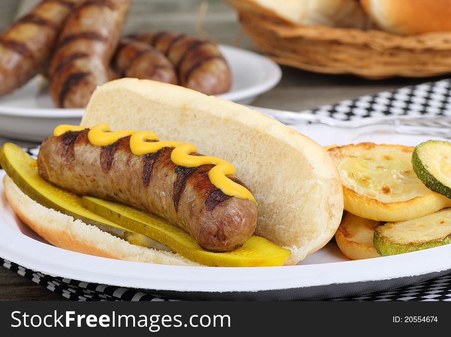 Grilled bratwurst with mustard and pickles on a bun and fried squash. Grilled bratwurst with mustard and pickles on a bun and fried squash