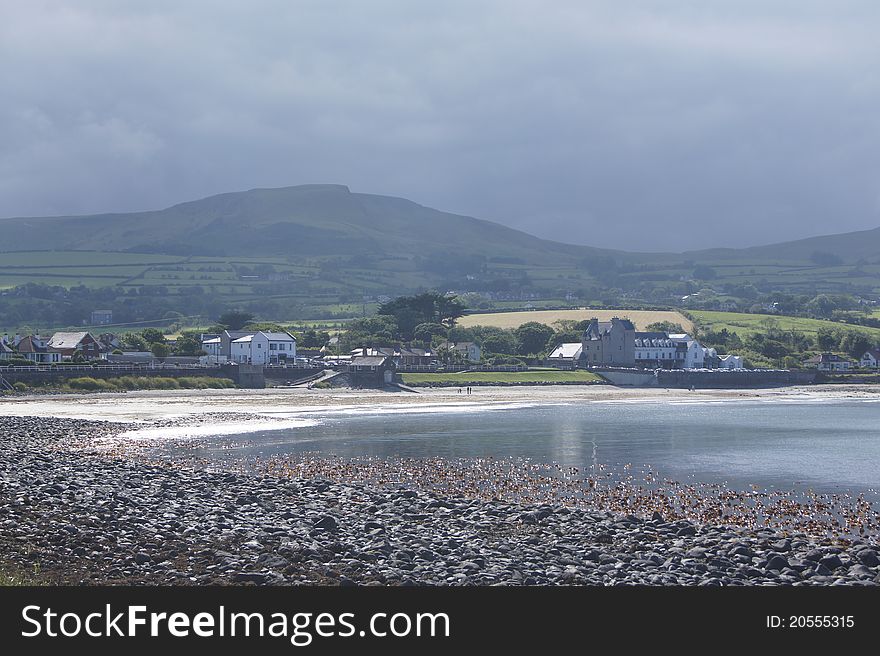 I shot of Ballygally beach with the sun shining on the water and sand but dark forboding clouds coming from the hills.