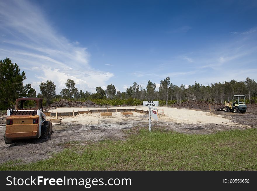 New Foundation, Footings. New construction site with wood framed footings, sand base. Earth movers in foreground and background. For Sale.