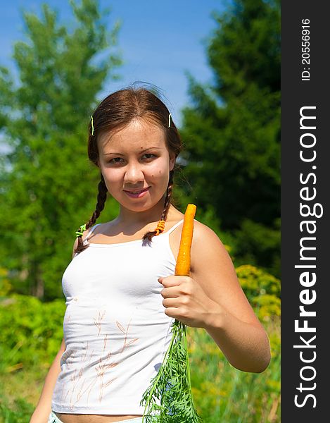 Young smiling woman holds fresh orange organic carrot in garden. Young smiling woman holds fresh orange organic carrot in garden