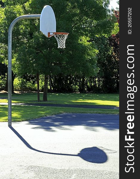 Basketball court outdoor early morning summer sun in a public park surrounded by trees. Basketball court outdoor early morning summer sun in a public park surrounded by trees.