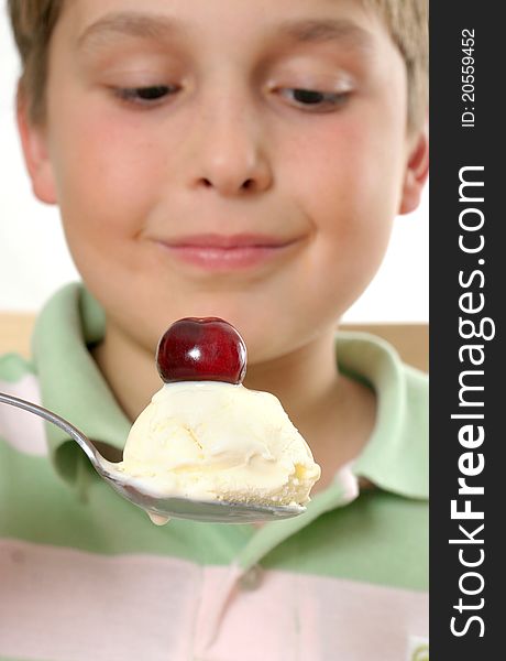 Boy scooping up and holding a spoonful of creamy ice cream with a cherry on top. Selective focus. Boy scooping up and holding a spoonful of creamy ice cream with a cherry on top. Selective focus.