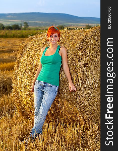 Smiling young woman standing near a straw roll on the wheat field. Smiling young woman standing near a straw roll on the wheat field