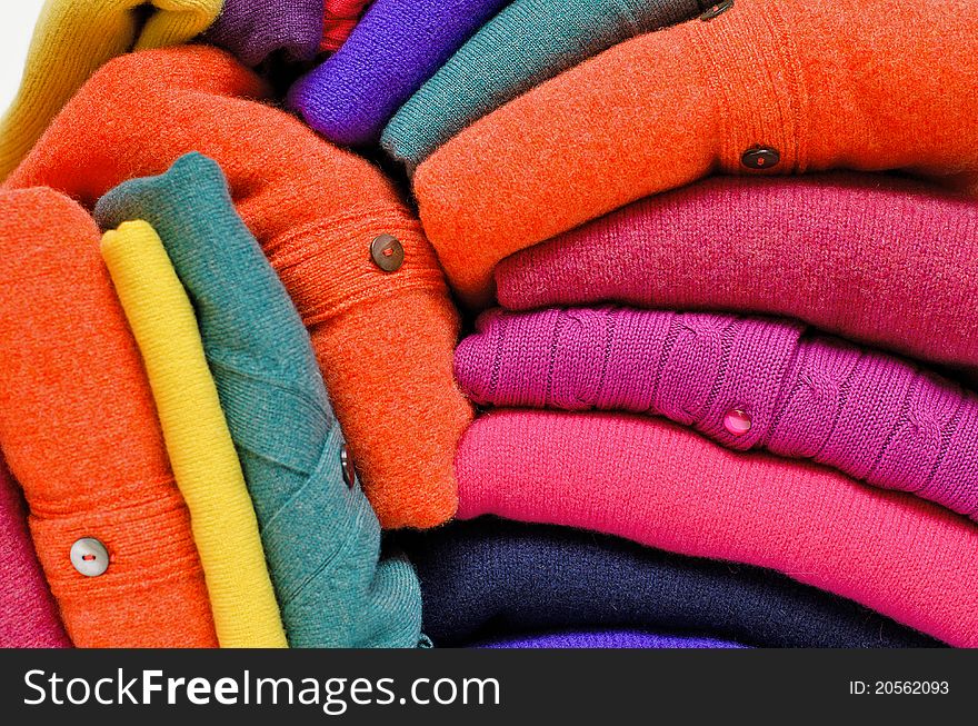 Stack of women's sweaters and cardigans in bright vivid colours against white in natural woolen fibers. Stack of women's sweaters and cardigans in bright vivid colours against white in natural woolen fibers.