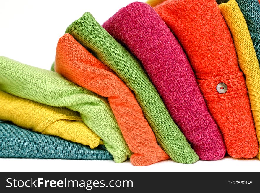 Stack of women's sweaters and cardigans in bright vivid colours against white in natural woolen fibers. Stack of women's sweaters and cardigans in bright vivid colours against white in natural woolen fibers.