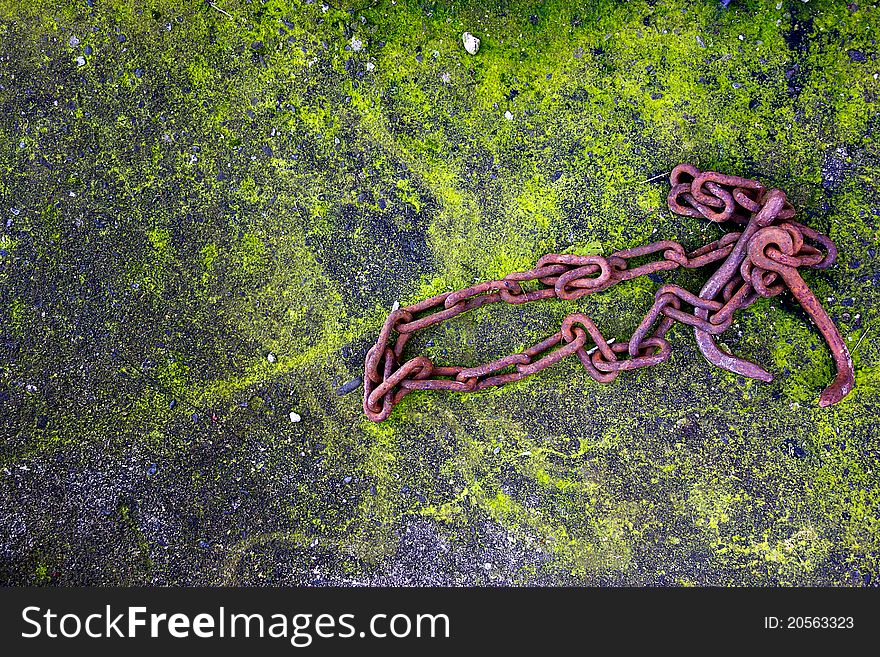 Rusty metal chain on moss-covered concrete.