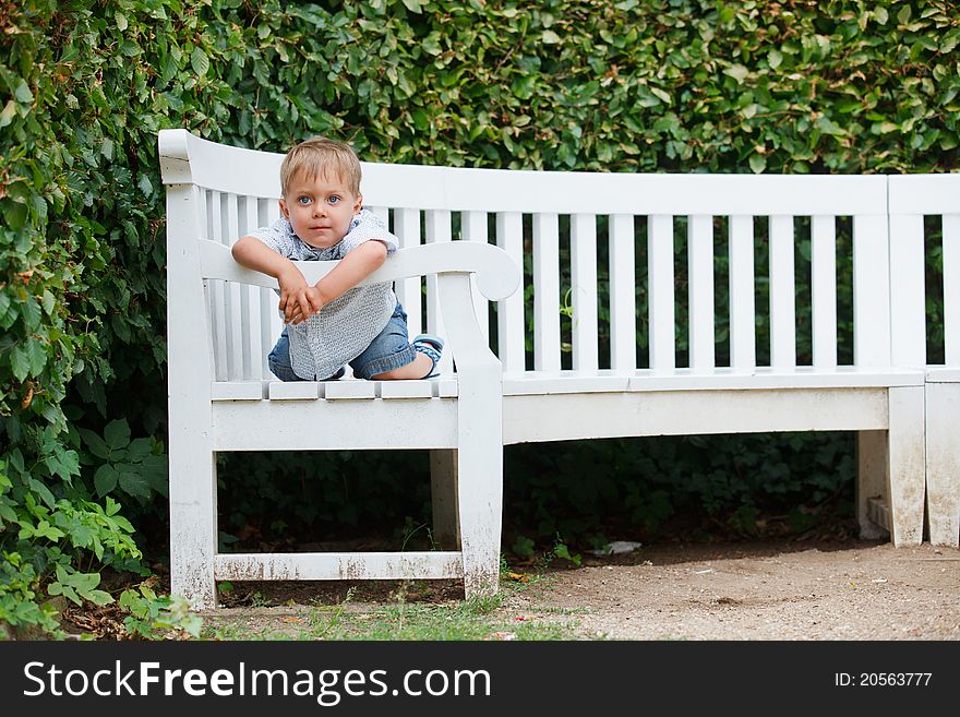 Little Boy Sits On A Bench In A Park