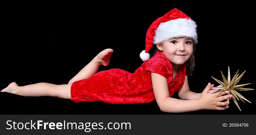 Sweet little girl in santa hat laying on floor with golden Christmas star. isolated on black. Sweet little girl in santa hat laying on floor with golden Christmas star. isolated on black