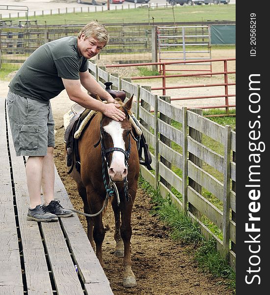 A mid-aged city-man petting a gentle horse in preparation for a guided trail ride. A mid-aged city-man petting a gentle horse in preparation for a guided trail ride.
