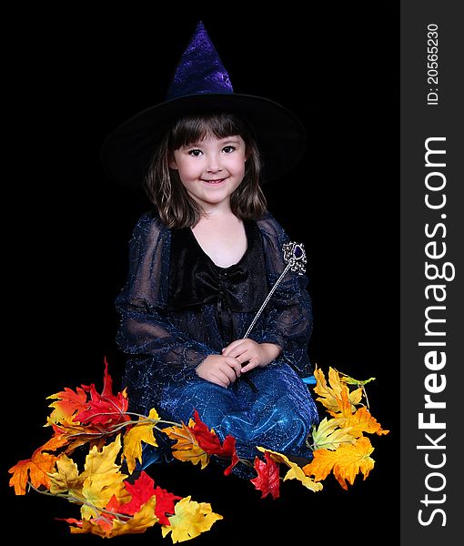 Little girl in witch costume surrounded by fall leaves and smiling. isolated on black. Little girl in witch costume surrounded by fall leaves and smiling. isolated on black