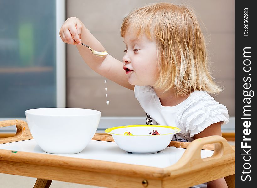 A small girl is sitting on the floor and is eating. A small girl is sitting on the floor and is eating