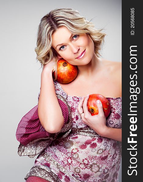 Portrait of beautiful blonde woman holding two pomegranates on grey background. Portrait of beautiful blonde woman holding two pomegranates on grey background